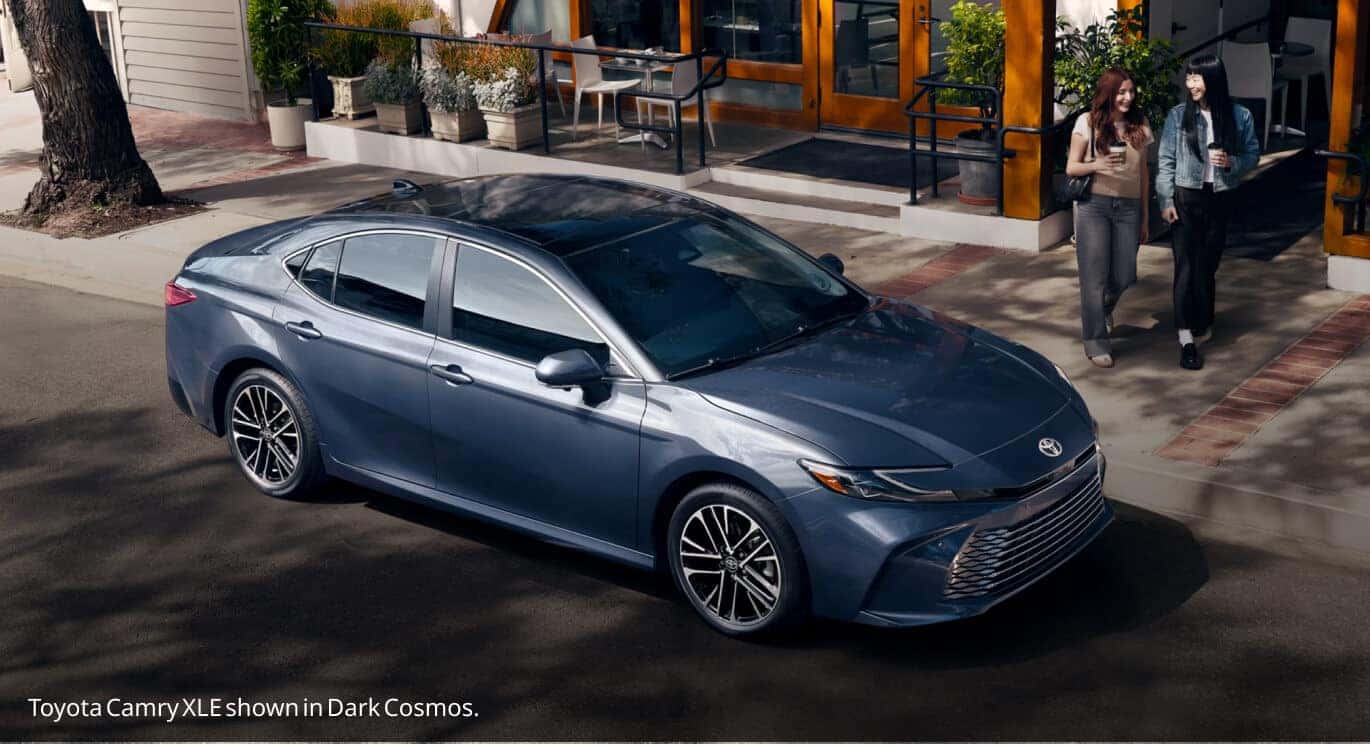 High-angle front three-quarter view of a Dark Cosmos Toyota Camry XLE parked curbside near a sidewalk café.