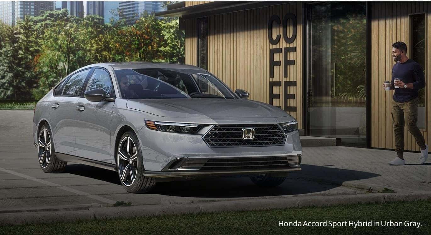 Front three-quarter view of an Urban Gray Honda Accord Sport Hybrid parked outside a modern wood-paneled coffee shop.
