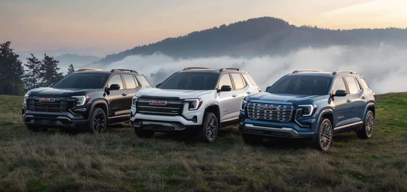 Exterior shot of three 2025 GMC Terrain trim levels parked side-by-side in a grassy mountain clearing.