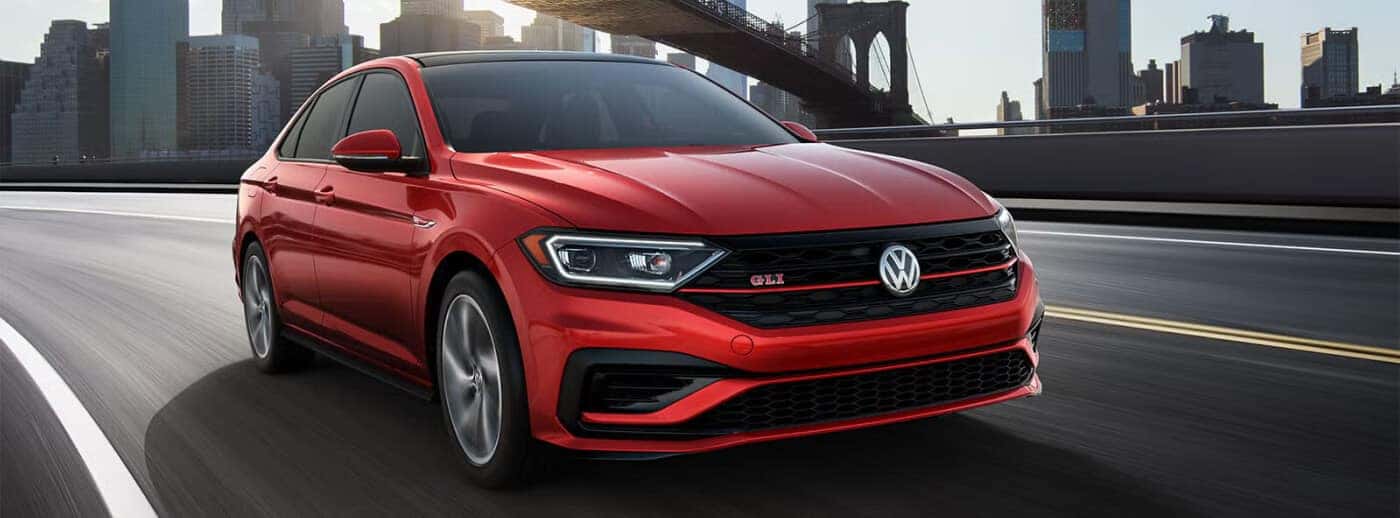 Low angle action shot of a red 2020 VW Jetta GLI driving down a city highway.