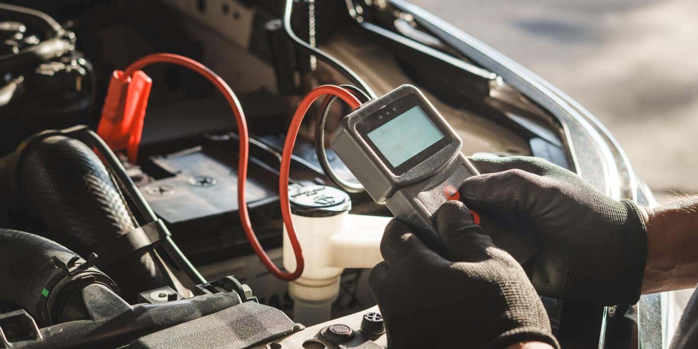 Close-up shots of a pair of gloved hands holding a voltage meter connected to a car battery.