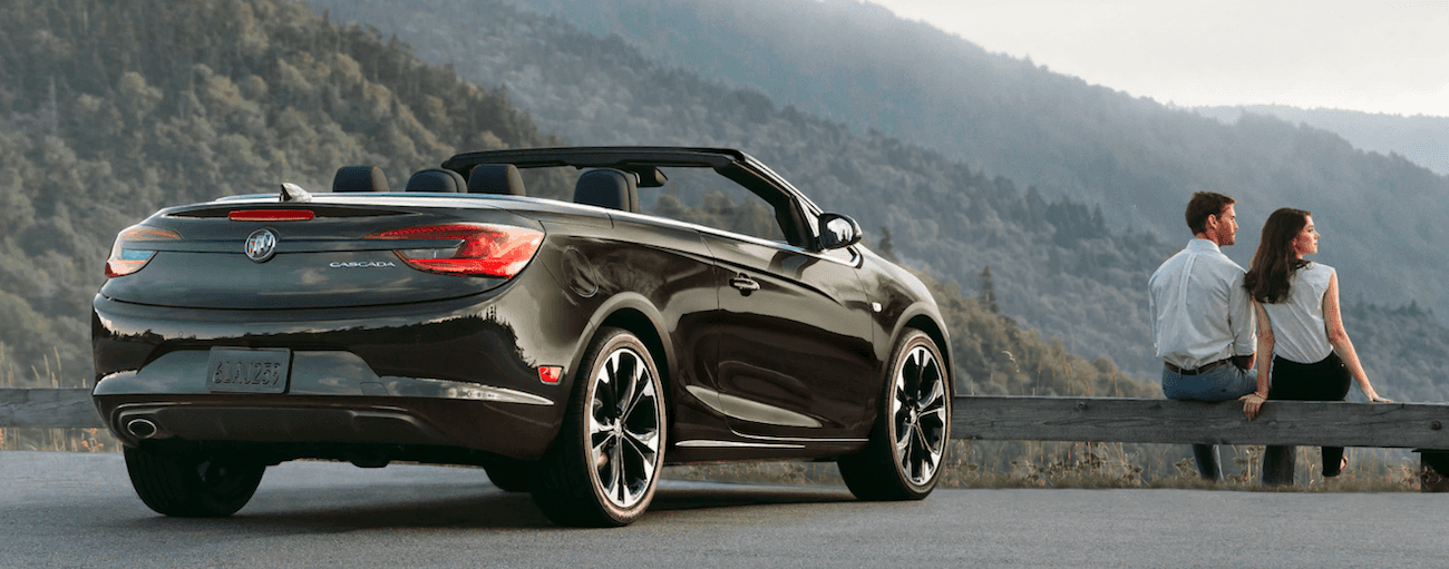 Black 2019 Buick Cascada on mountain, man and woman sitting on guardrail