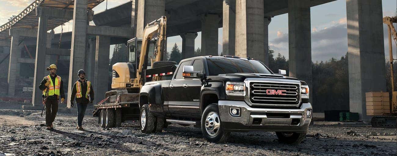 Black 2019 GMC Sierra 3500HD with tractor on trailer, construction workers