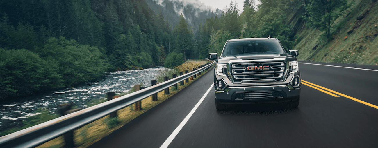 Black 2019 GMC Sierra 1500 driving towards camera next to woodland river