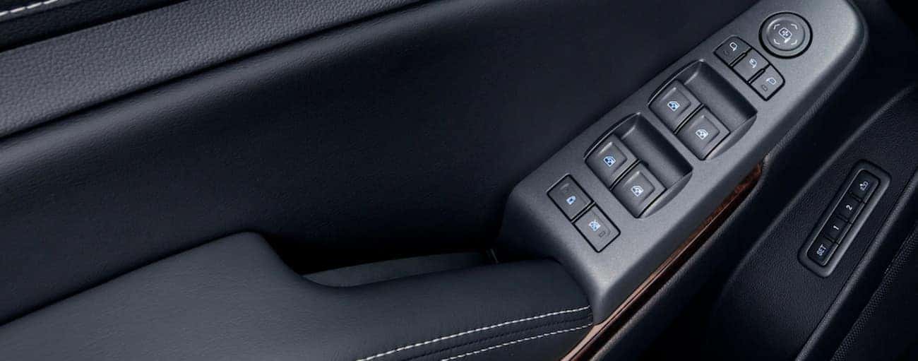 Black plastic and leather interior with wood accents of 2019 GMC Yukon, closeup of controls on door