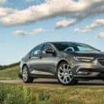 A silver 2019 Buick Regal navigates a twisty grass field lined road