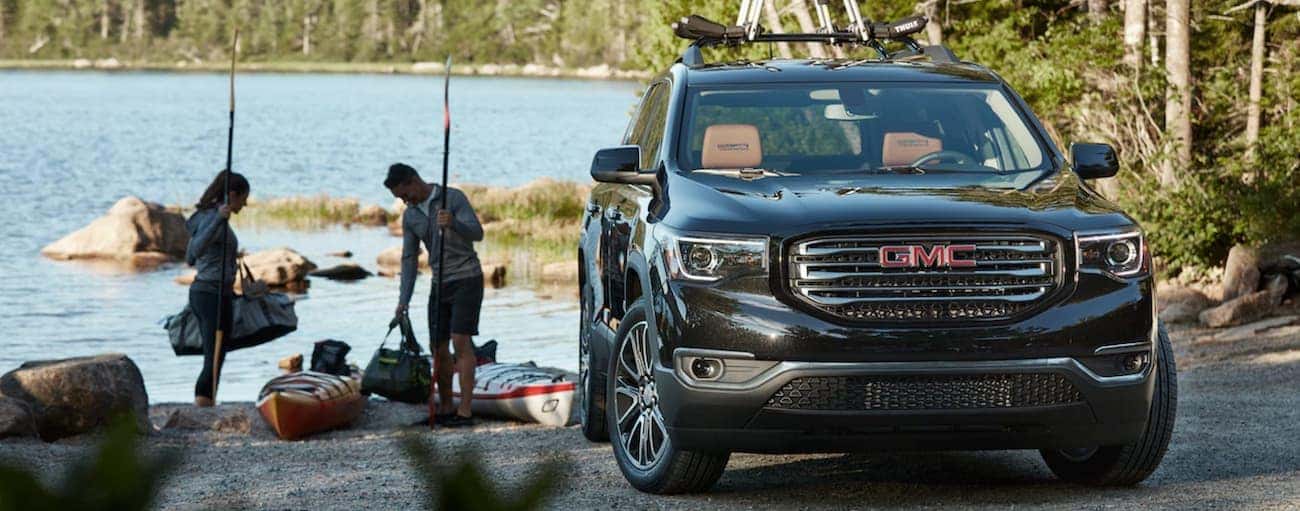 A couple unpacks their kayaks at a lake with their black 2019 GMC Acadia