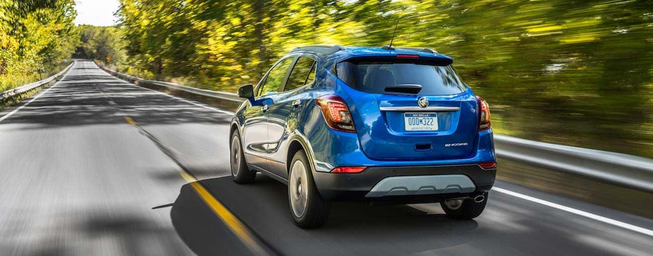 A blue 2019 Buick Encore drives down a tree-lined road with the win of  2019 Buick Encore vs 2019 Mazda CX-3