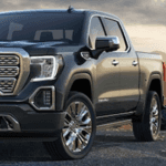 Front driver angle of a blue 2019 GMC Sierra parked outdoors with a sunset in the background