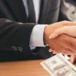 Salesman-and-woman-shaking-hands-over-wood-table-in-car-dealership