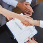 salesperson shaking hands with couple over paperwork