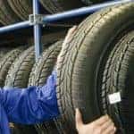 a man holding a vehicle tire by a rack of tires