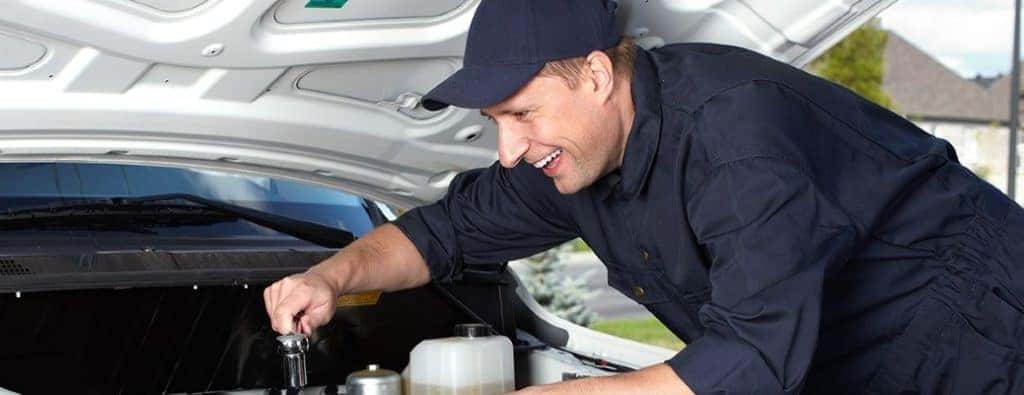 a happy worker looking under the hood of a car