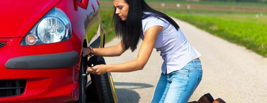 A woman putting a spare tire on a red car