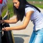 A woman putting a spare tire on a red car