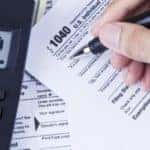 A hand holding a pen to a tax document