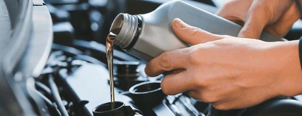 hands holding a bottle of oil pouring it into a car engine