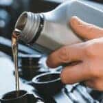 hands holding a bottle of oil pouring it into a car engine