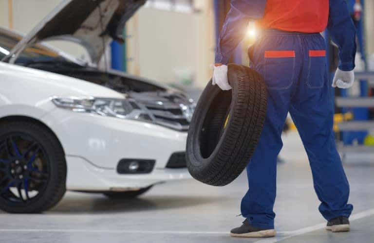 a man holding a tire by a white car