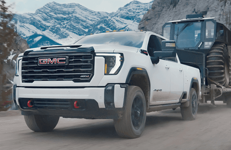 a white 2024 GMC Sierra HD truck pulling a trailer in the mountains