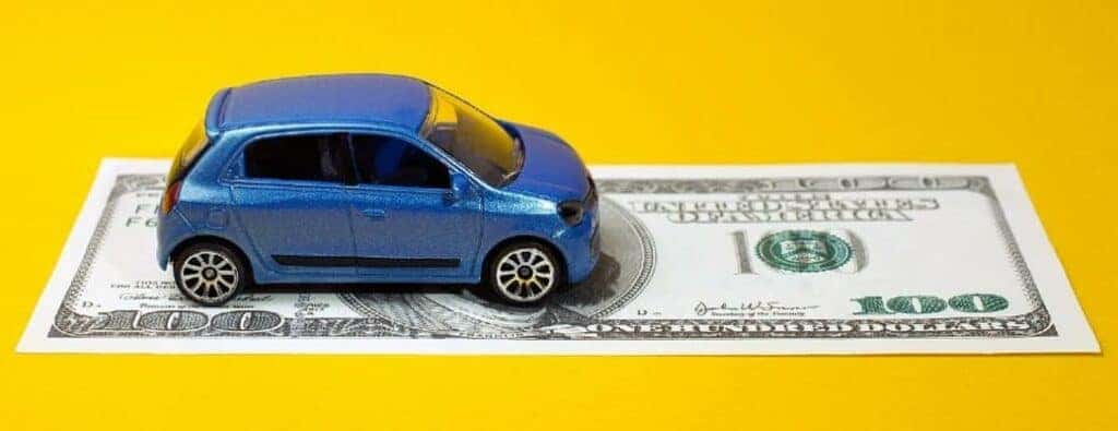 a blue toy car driving on a dollar bill on a yellow surface