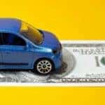 a blue toy car driving on a dollar bill on a yellow surface