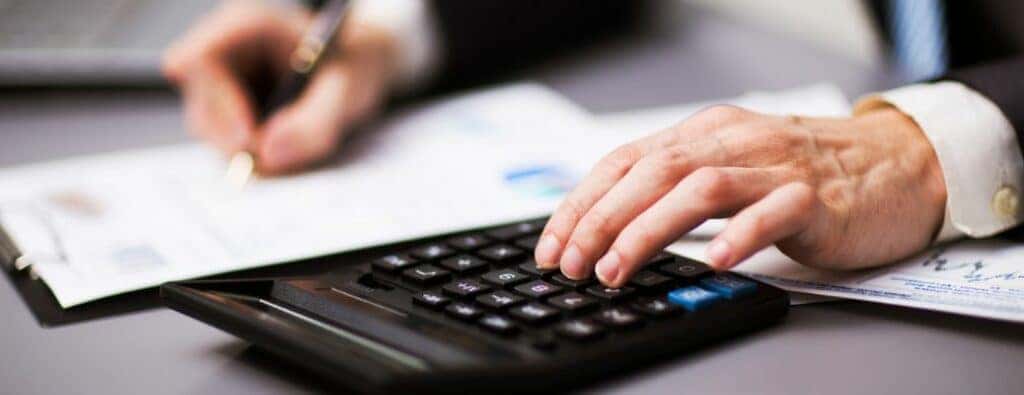 one hand typing on a calculator while another writes on a form
