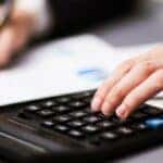 one hand typing on a calculator while another writes on a form