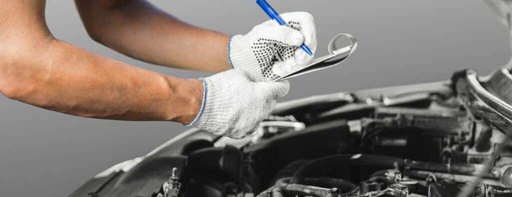 two white-gloved hands writing on a paper over a car engine