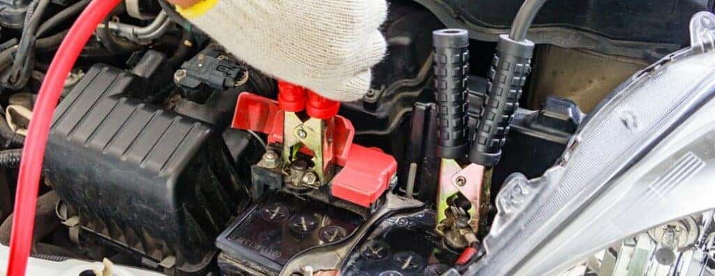 a white-gloved hand attaching jumper cables to a car