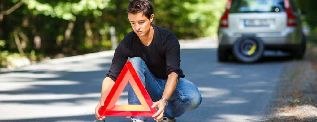 a person crouched in a road holding an orange triangle