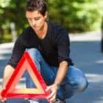 a person crouched in a road holding an orange triangle