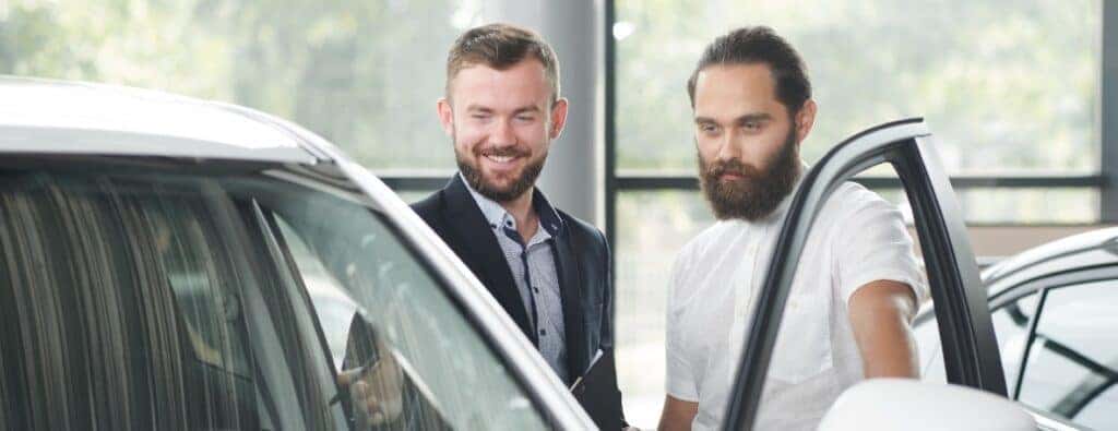 two men looking into the driver's door of a white car
