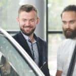 two men looking into the driver's door of a white car
