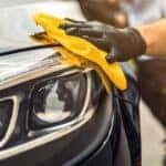 a black-gloved hand using a yellow sponge to clean a car headlight