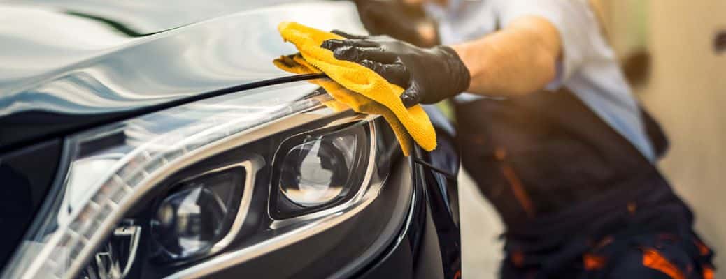 a black-gloved hand using a yellow sponge to clean a car headlight