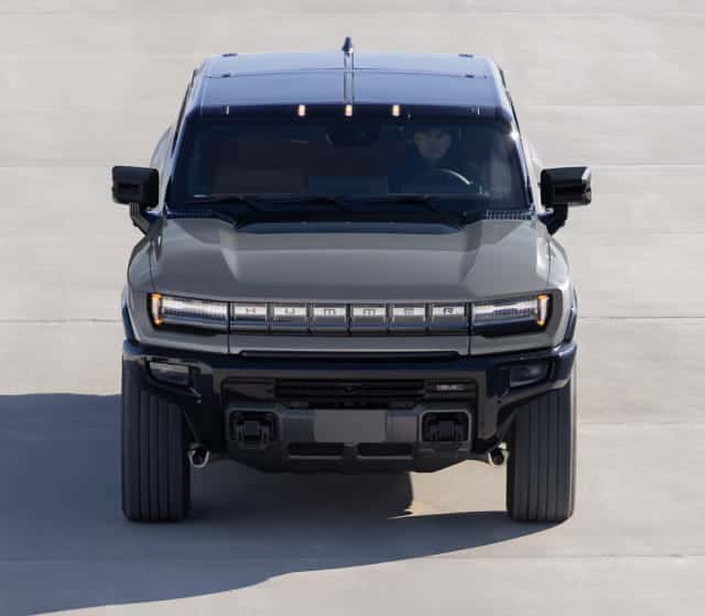 Front view of a the 2026 Hummer EV SUV with bold, angular design against a blue textured wall
