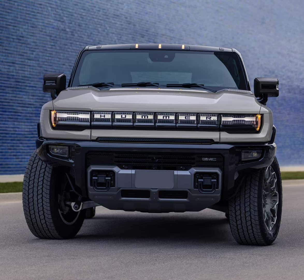 Front view of a the 2026 Hummer EV SUV with bold, angular design against a blue textured wall.