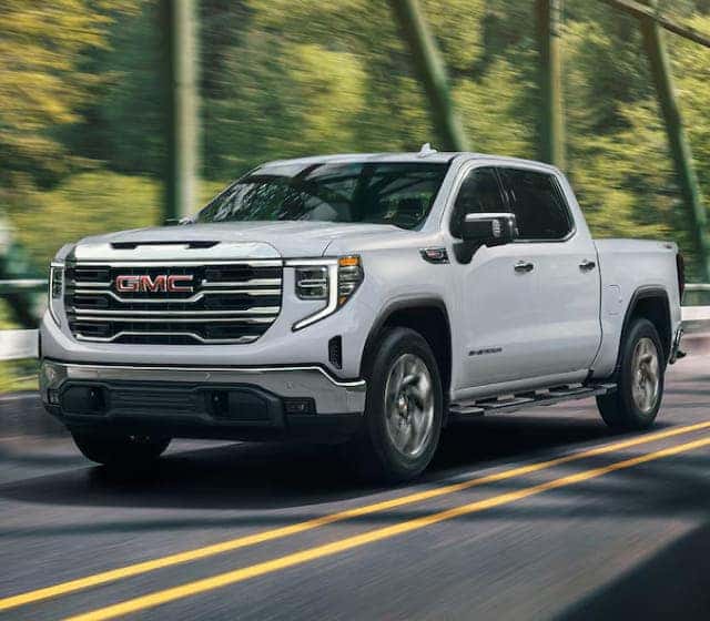 2026 GMC Sierra 1500 truck drives across a bridge with blurred trees in the background.