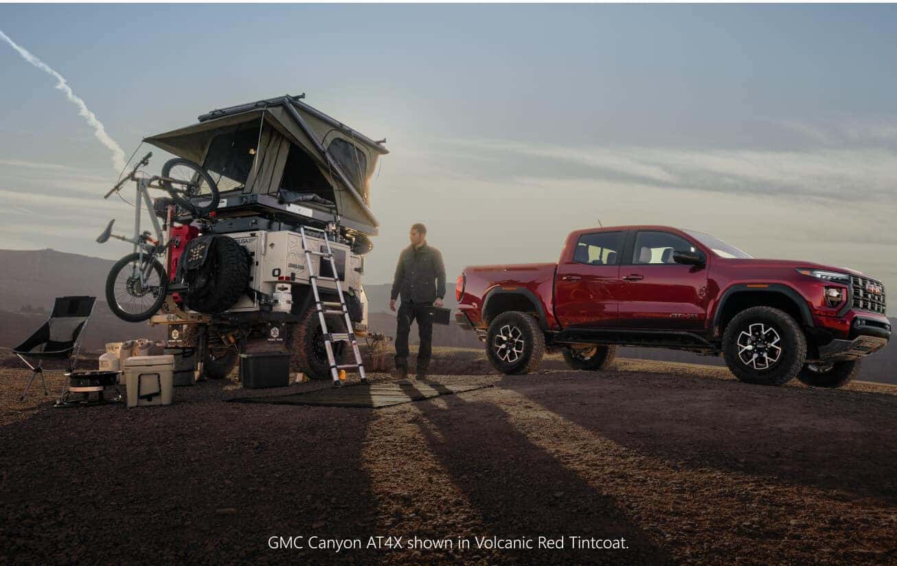 Front three-quarter view of a red GMC Canyon AT4X parked next to an overlanding camping trailer.