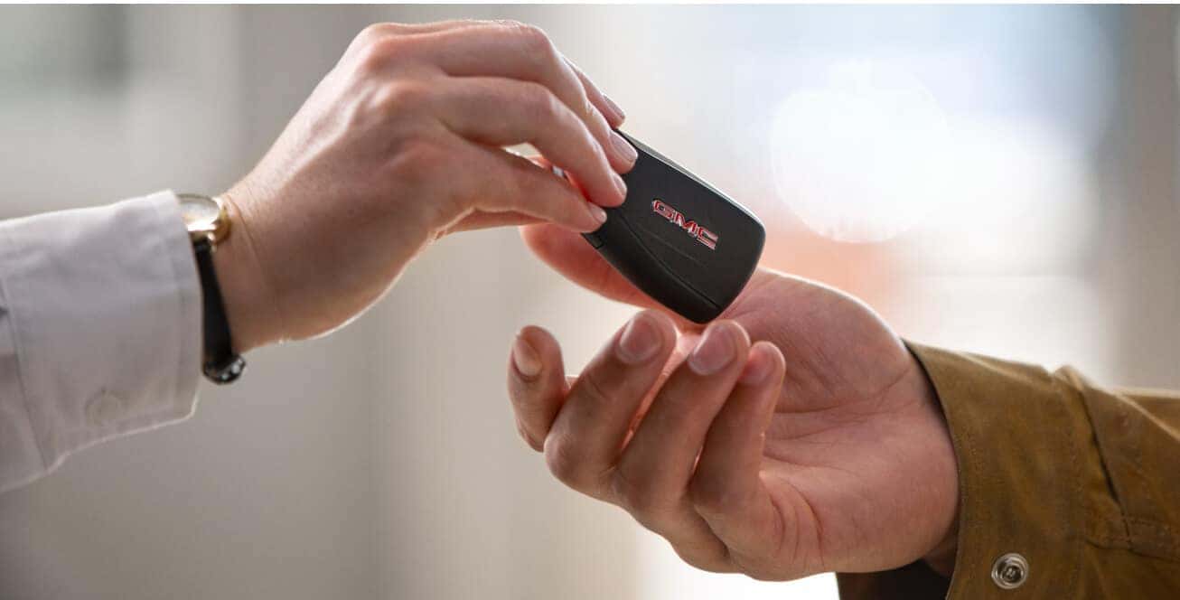 Close-up view of a dealership representative handing over a black GMC key fob to a customer.