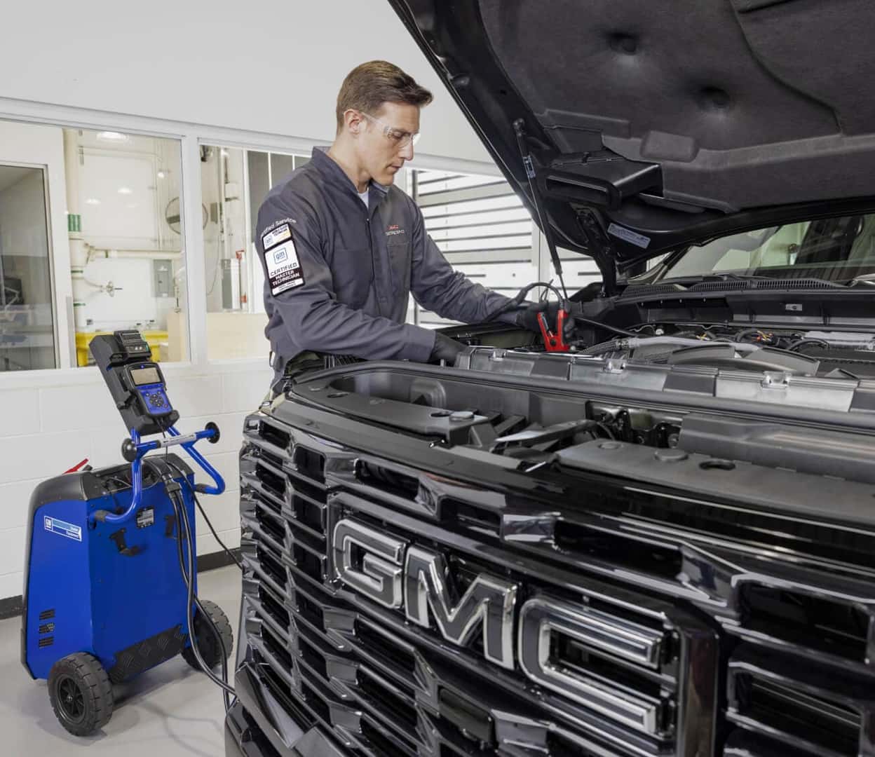 Front view of a GMC master technician diagnosing a black GMC truck engine bay with electrical equipment.
