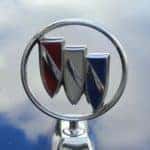 Closeup of the Buick 3 shield logo on a hood of a blue car