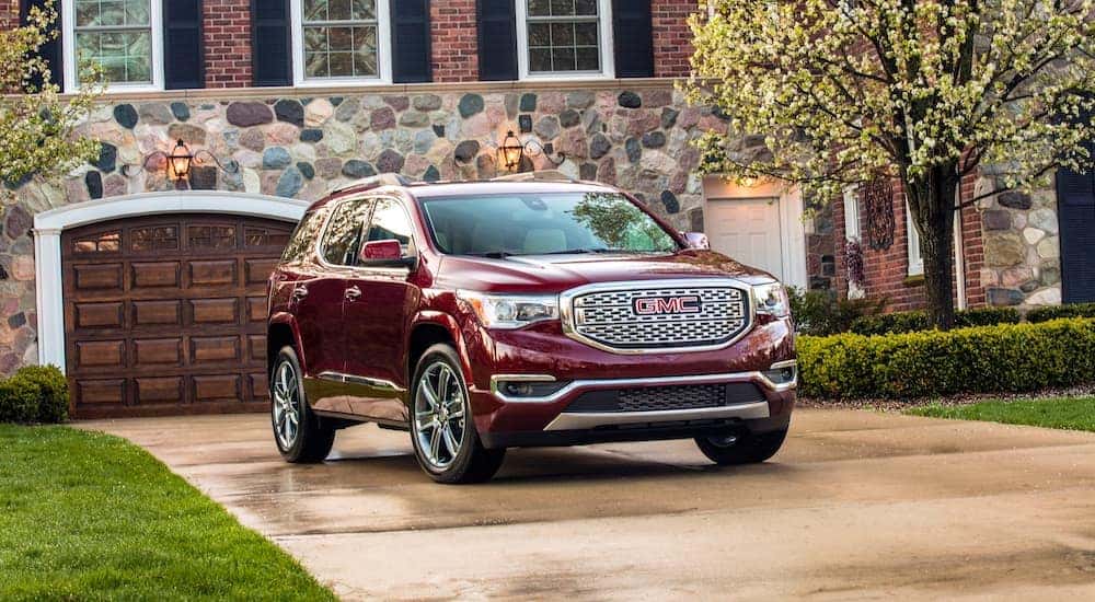 A red 2019 GMC Acadia Denali in front of a house with a stone facade