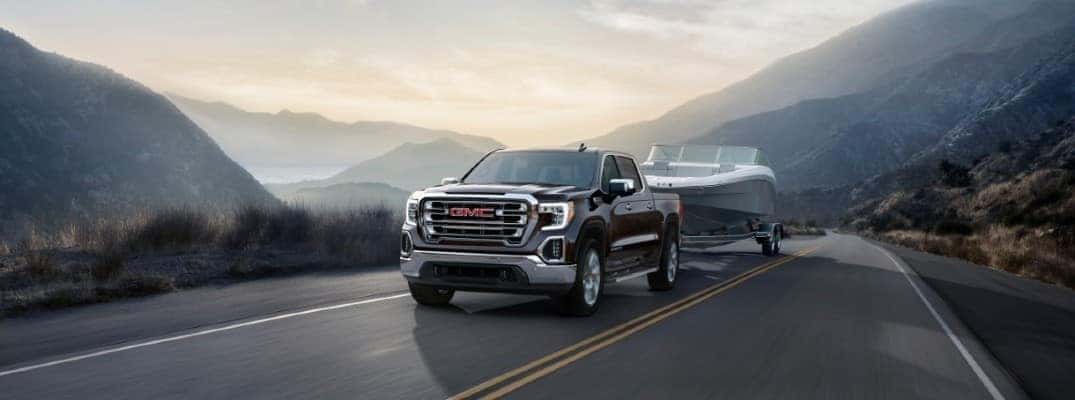 2020 GMC Sierra 1500 driving down the road at sunrise, towing a trailer