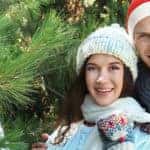 A man and a woman standing next to a pine tree wearing winter hats