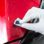 Person scrupping at hood of red car with small cloth