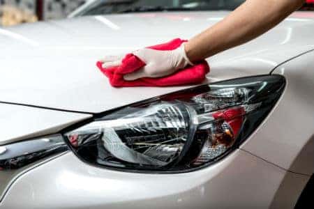 Person wiping hood of white car with red cloth