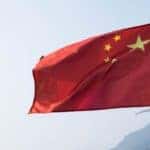 A Chinese flag blows against a clear sky.