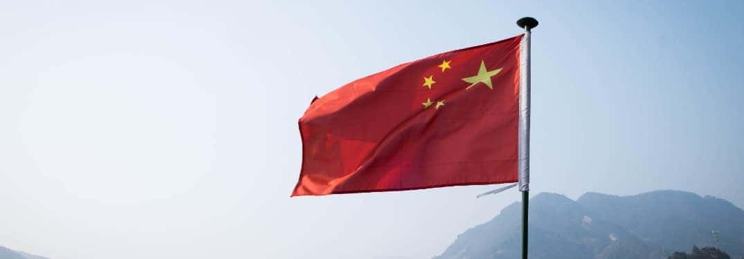 A Chinese flag blows against a clear sky.